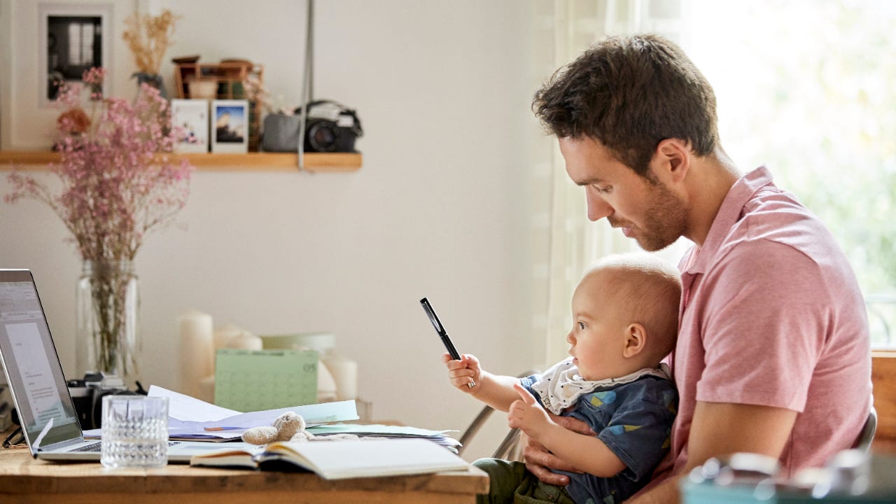 A father holds his infant son in front of a computer